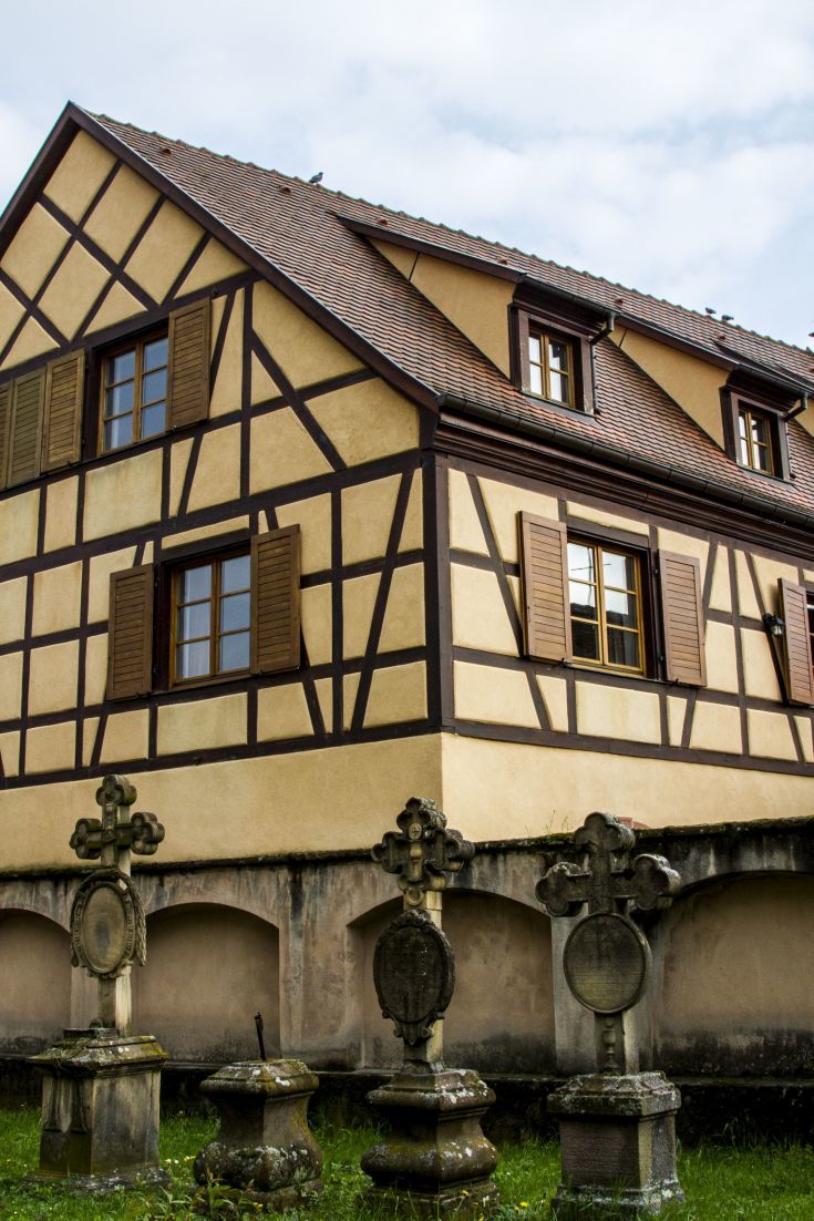 Cream colored half-timbered house overlooking an ancient cemetery in Alsace.