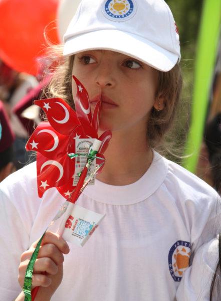 A girl holds a pinwheel of Turkish flags.