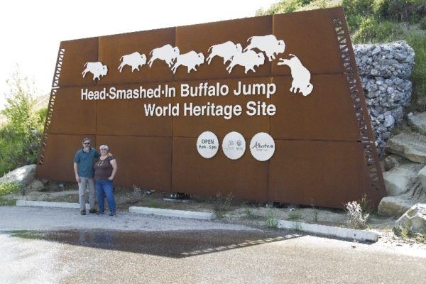 Jim and Corinne pose in front of the sign at Head-Smashed-In Buffalo Jump, Canada.