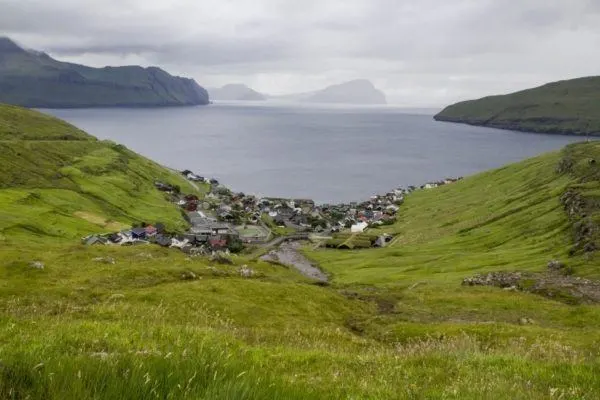Looking down a grassy slope to a fishing villages nestled in a bay on the Faroe Islands.