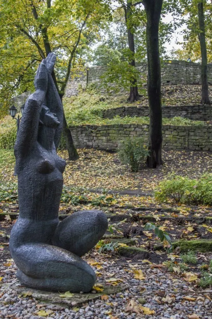 Fall colors blanket the ground around a kneeling lady statue in Riga.
