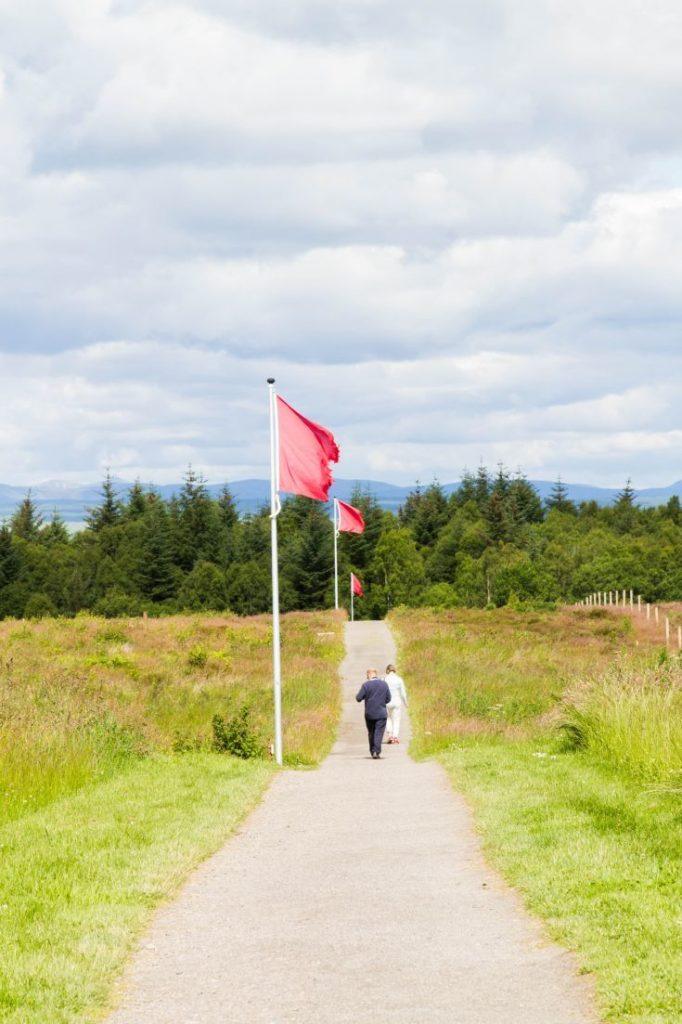 A couple walk past Red flags flying over the Battlefield of Culloden.