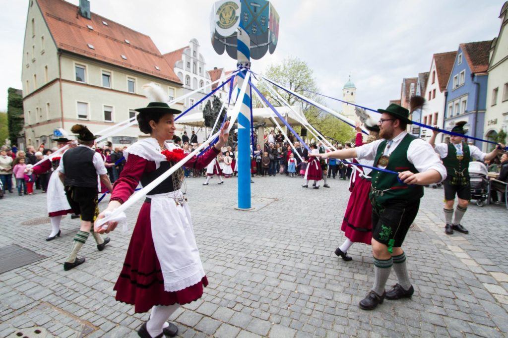 Dancers in traditional Bavarian clothes dance around the Maypole.
