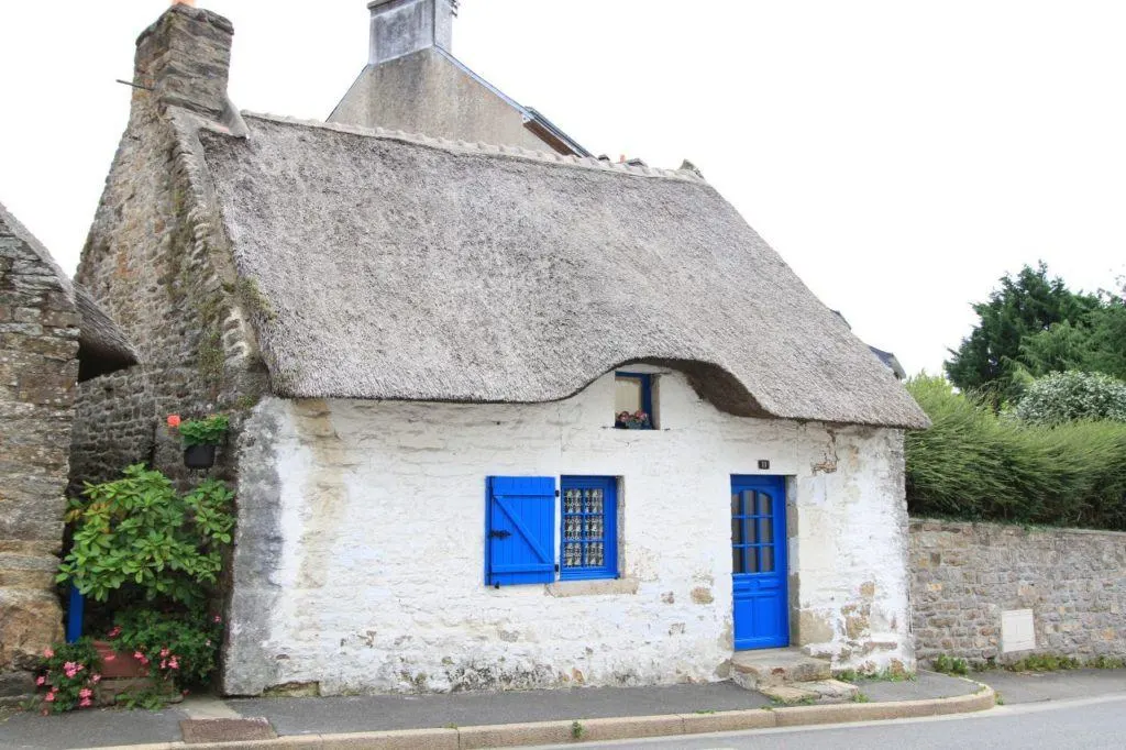 Adorable white-washed stone cottage with thatched roof and bright blue doors adds to the charm of another quaint French village.
