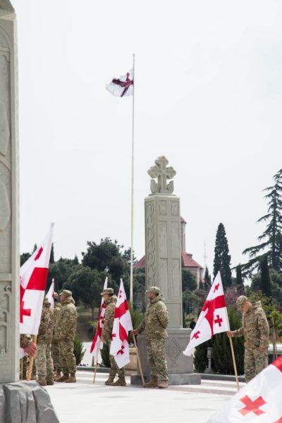 Georgian soldiers holding national flags during military memorial ceremony.
