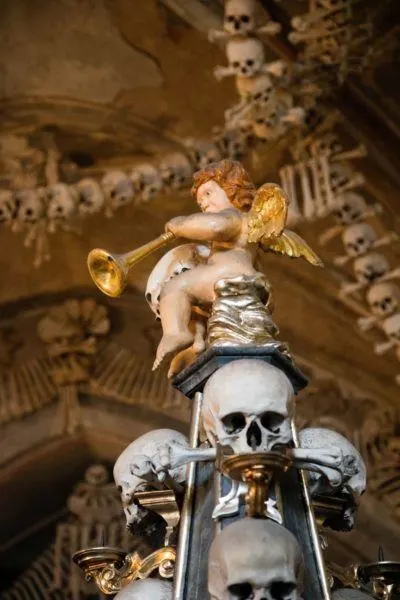 Cherub angel with horn atop skull pillar.