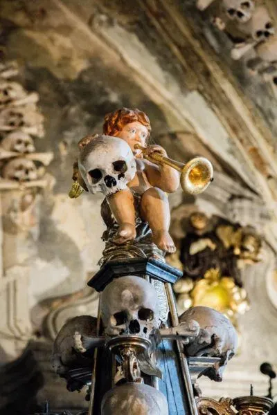 Closeup of angel playing horn and holding a human skull.