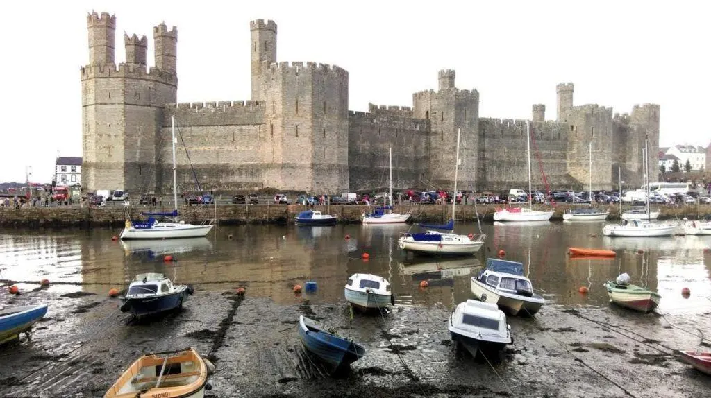 Small boats pulled up on the rocks in front of Caernarfon Castle in Wales.