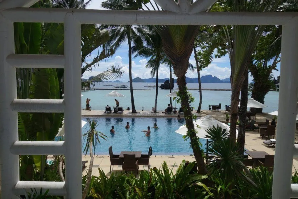 Tropical resort El Nido in Palawan, Philippines with a swimming pool, palm trees, beach front and fishing boats.
