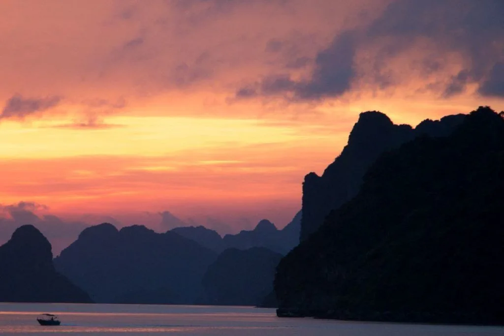 Sunset with a fishing boat and jagged cliffs on Halong Bay, Vietnam.