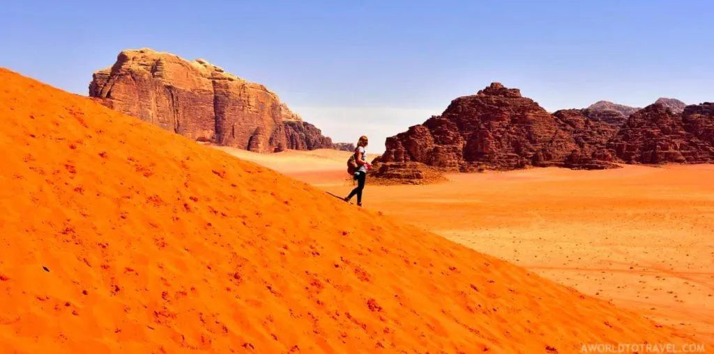 Woman walks down the slope of an orange sand dune in Wadi Rum.