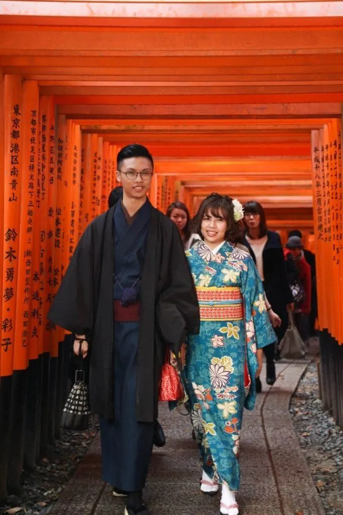 Young couple in traditional Japanese outfits walks through the Torii gate path.