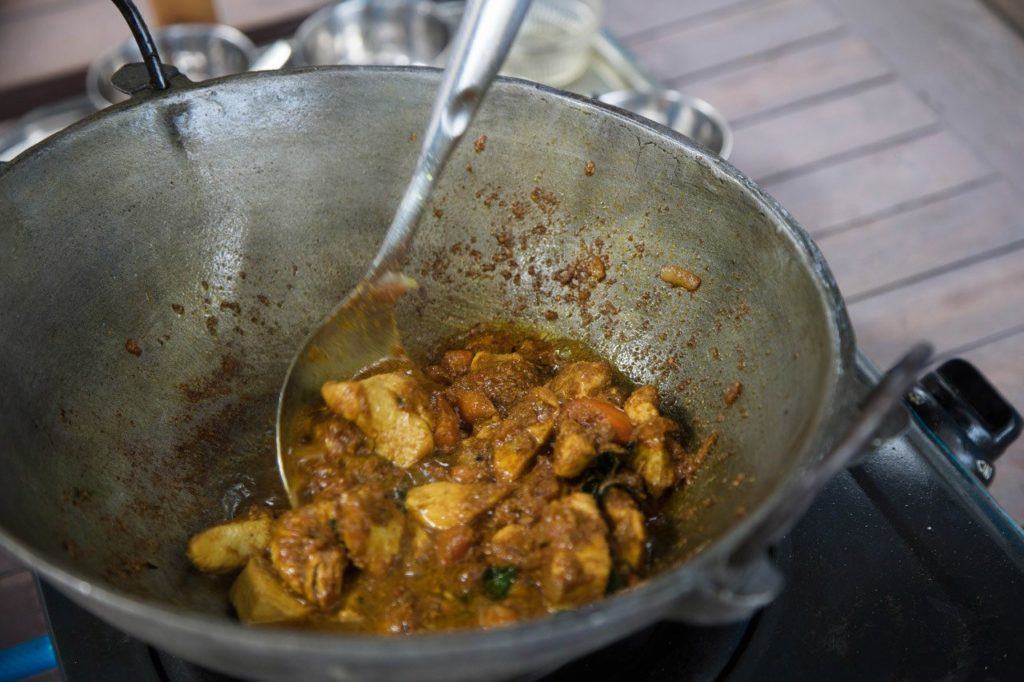 Cooking in a wok, traditional Mauritian chicken curry.