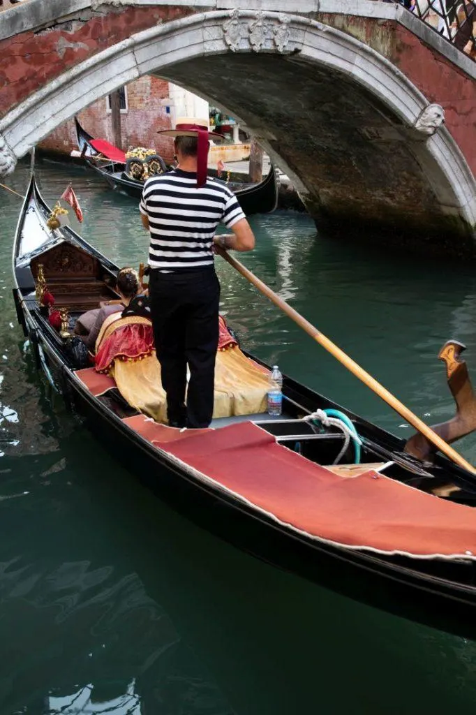 A traditional Venetian gondola goes under a bridge.