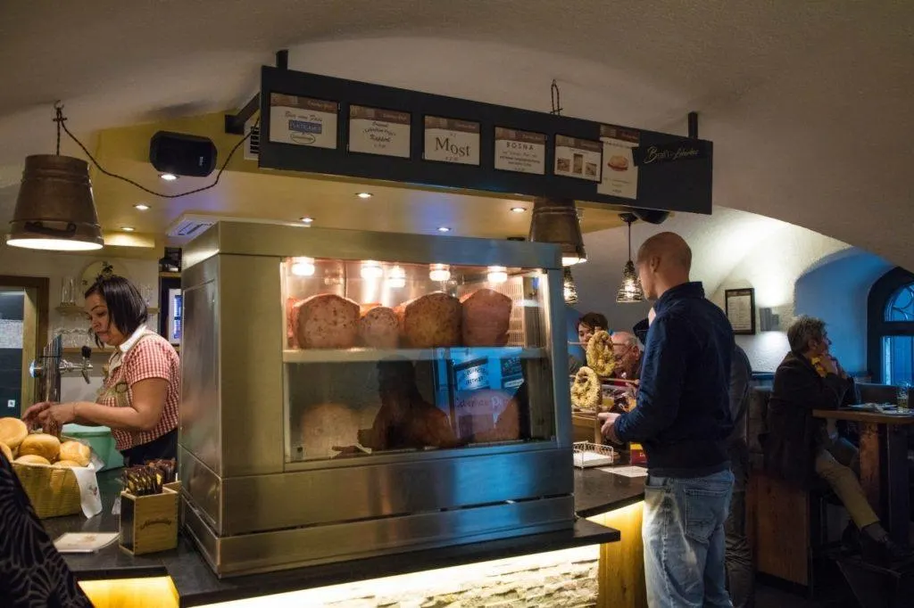 Interior of the leberkas restaurant with a waitress and customers around the display case.