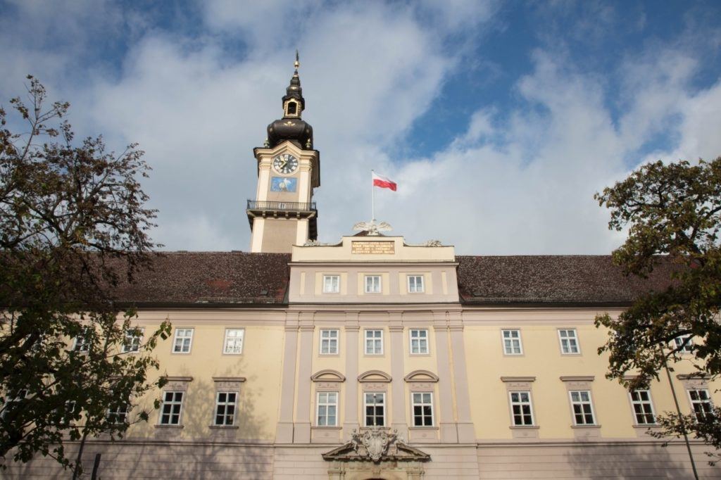 Large beige building with clock tower and Austrian flag.