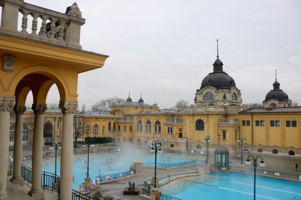 Yellow buildings, 2 pools, and steaming water in Budapest.