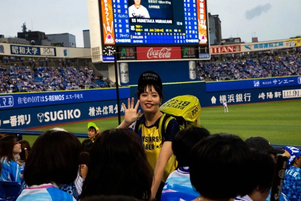 Young women carry a full keg of beer on their backs to sell to Japanese baseball fans. This girl is selling Baystars Beer, named after the team.