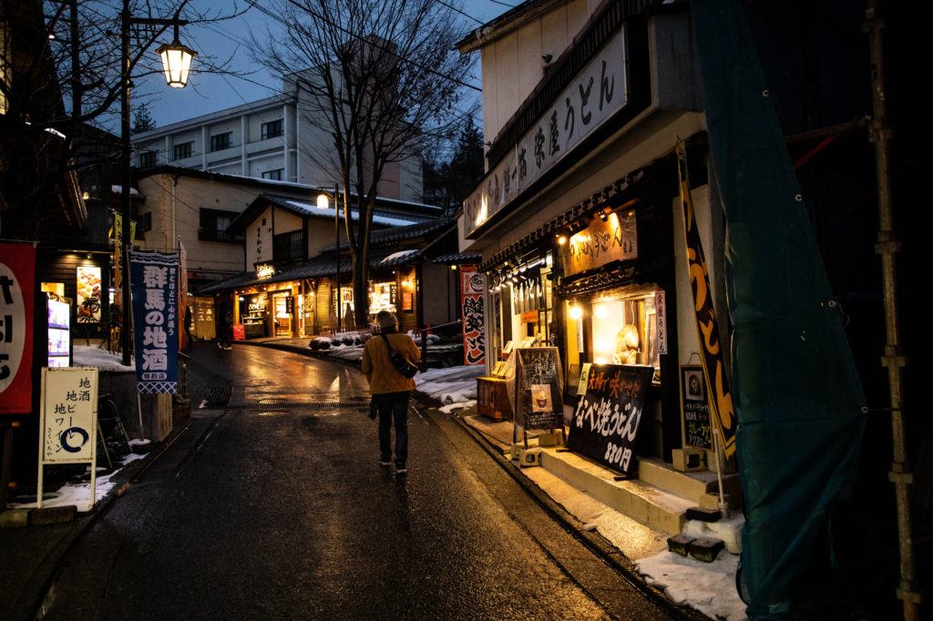 A tourist walks up a Kusatsu street at night.