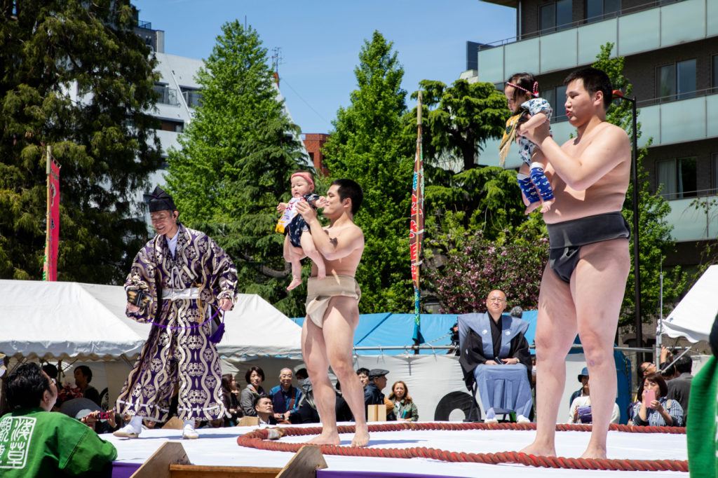 Young sumo wrestlers hold up 2 babies.
