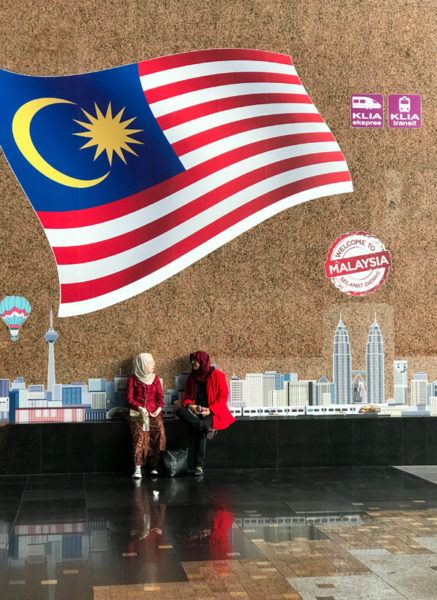 Two women sitting under Welcome to KL mural.