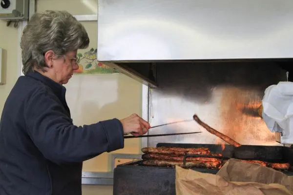 What to eat in Germany - Thuringer Sausages being cooked over a grill by an older lady.