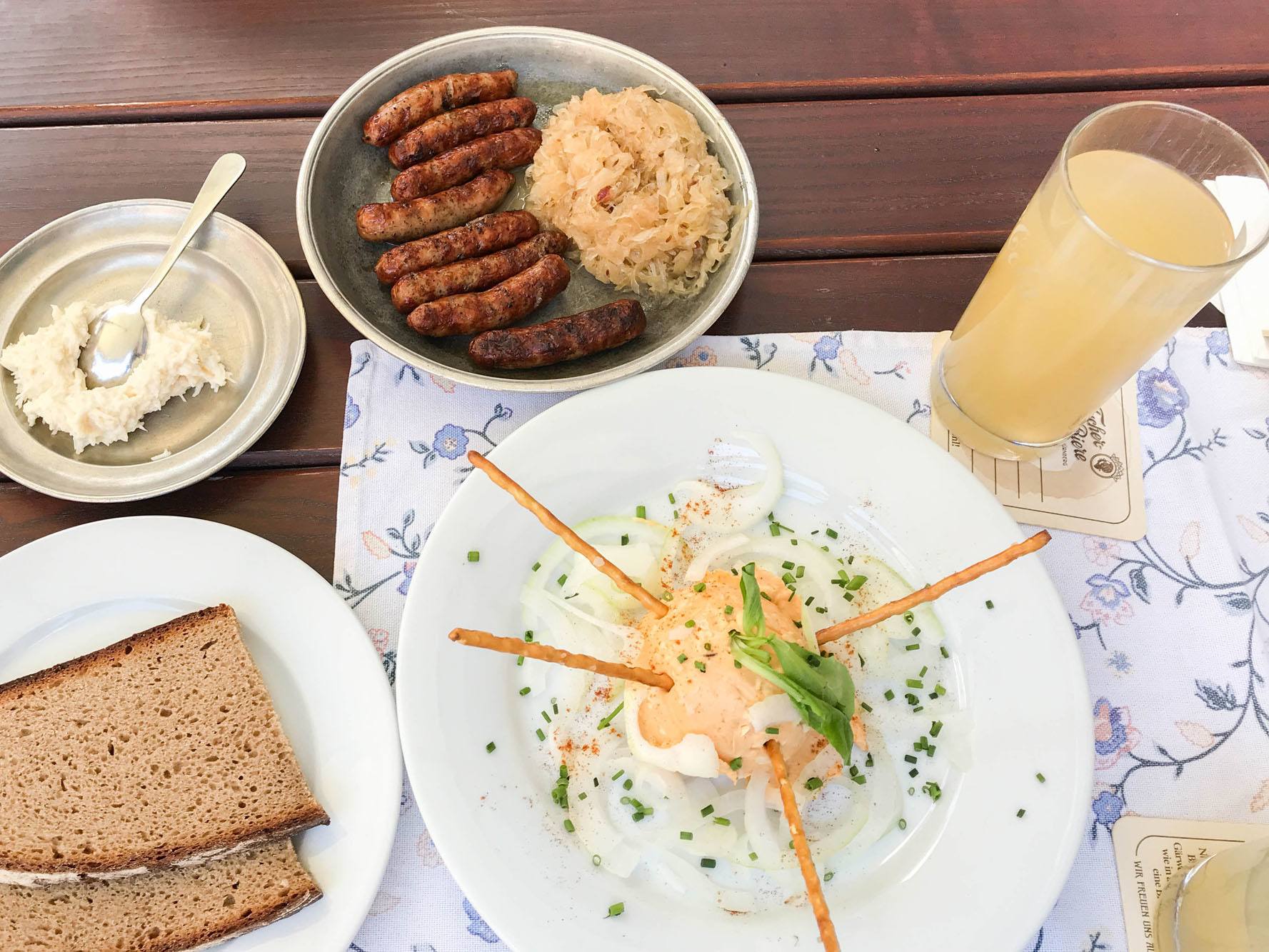 A Bavarian lunch of sausages, sauerkraut, Obatzda spread, and apple juice.