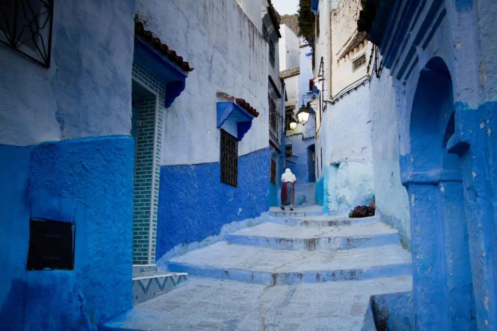 A woman walks through a narrow passage between the stunning blue-washed buildings in Chefchaouen, Morocco.