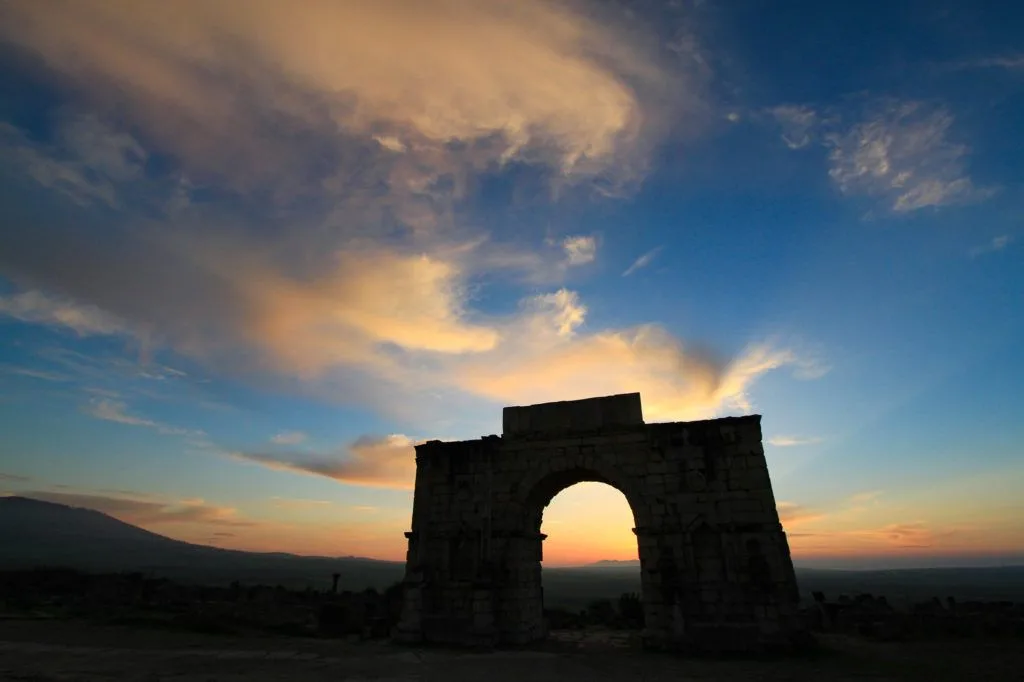 The sun is setting behind the Arch of Caracalla in the Roman ruins in Volubilis World Heritage Site, Morocco.