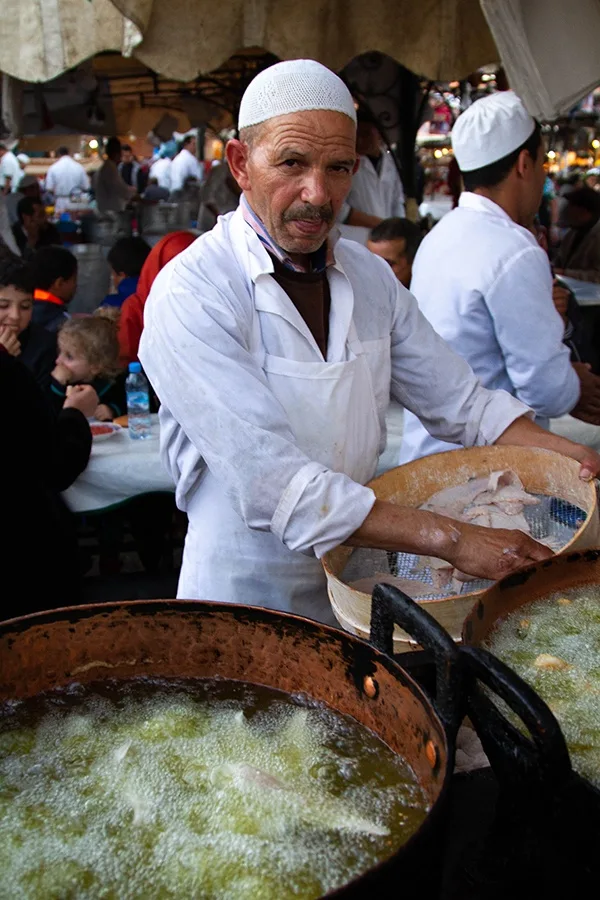A man deep frying fish filets at a food stall in Jemaa el Fna, Morocco.