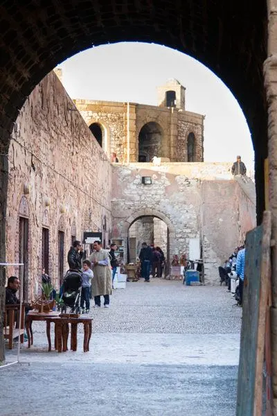 Looking through an arch into a passageway in the Essaouira city wall where men and a young boy appear to be shopping.