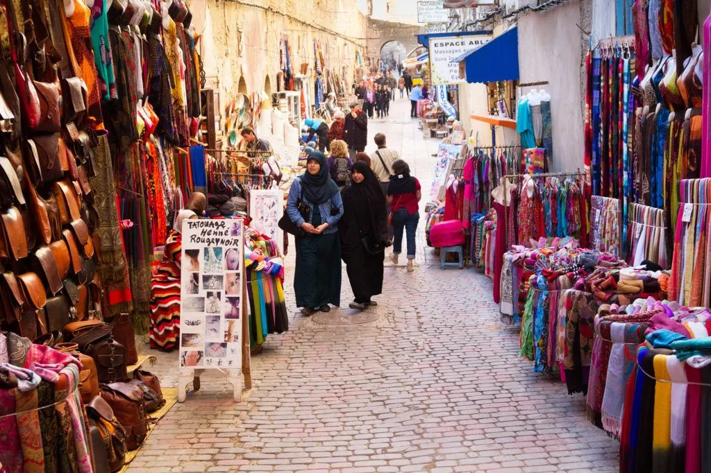 Women shopping at the stalls filled with brightly colored clothing and textiles in Le-Souk, in the Essaouira Medina.