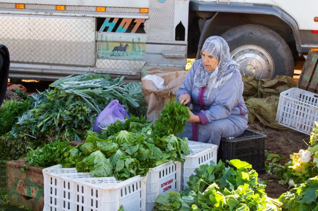 A women trims lettuce, herbs, and other vegetables at a Berber Market.
