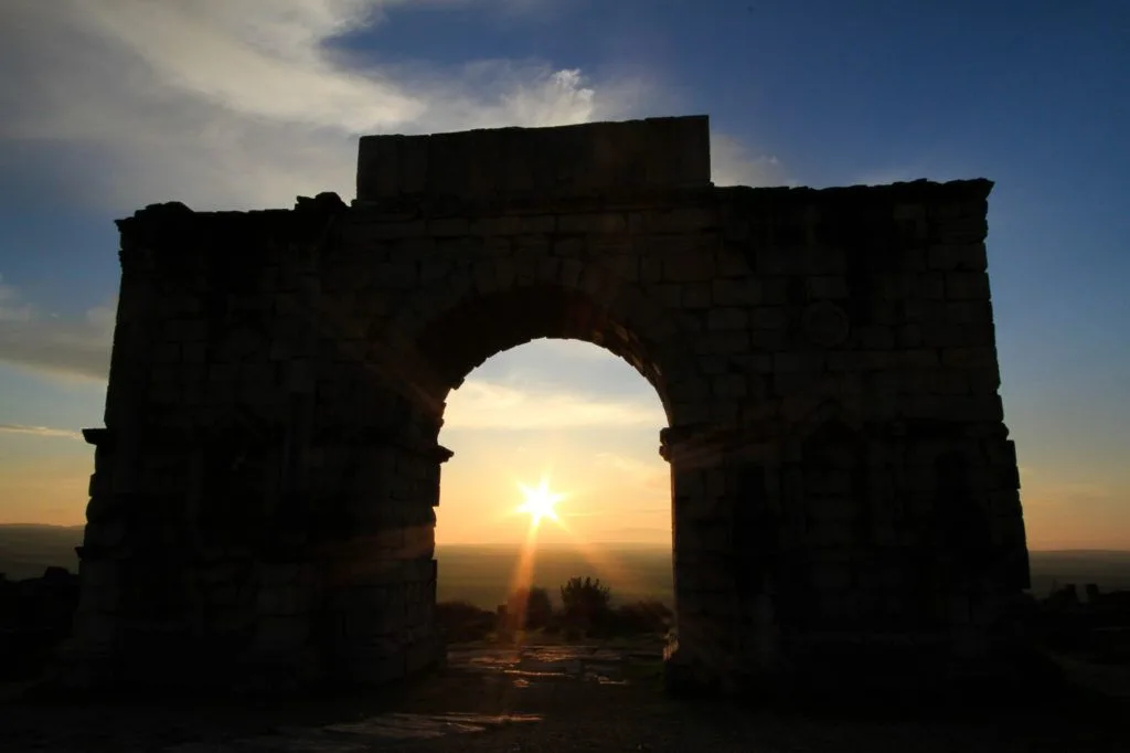 Setting sun shining through the triumphal Caracalla arch at the ruins in Volubilis, Morocco, A UNESCO World Heritage Site.