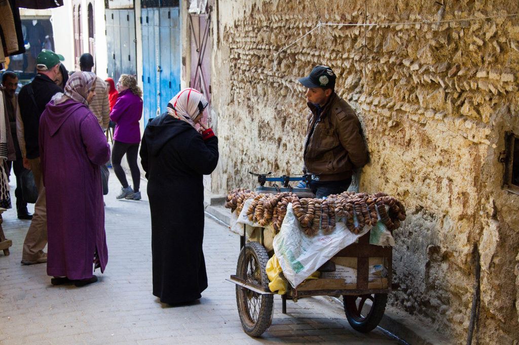 Two women stop to talk to a vendor selling dates in the Medina.