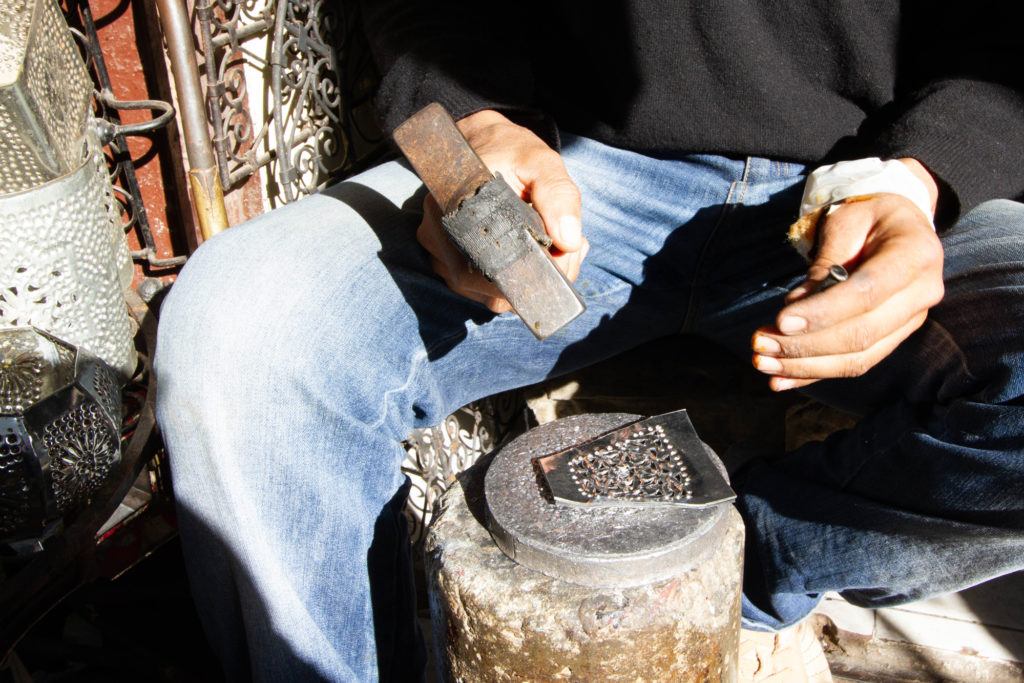 An artist in Marrakech uses a hammer and punch to create a piece of metal filigree.