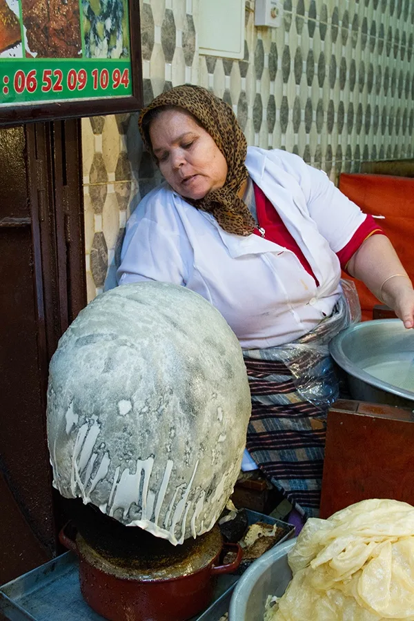 A lady makes thin bread by draping it of a ball.