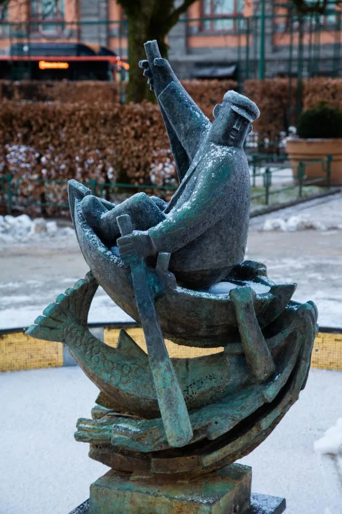 A statue of a fisherman rowing his boat glisten with bits of snow stuck to it on a Bergen Norway winter day.
