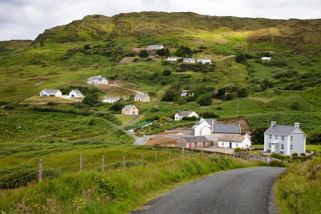 A narrow road winds through gorgeous green hills sprinkled with lovely white houses in County Donegal.