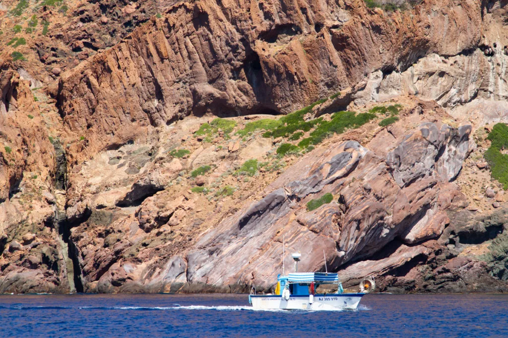 A fishing boat runs close to land in the Scandola Nature Reserve.