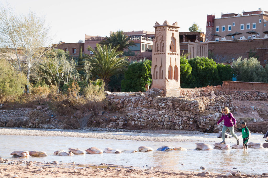 Lisa crosses the Ounila River with help from a young friend. Ait Benhaddou is one of the best places to go in the Atlas Mountains.