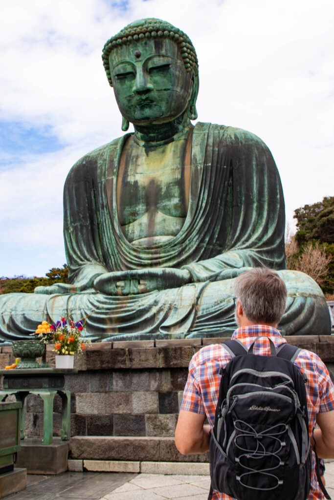 A day tripper with a day trip bag on his back standing before the Great Buddha in Kamakura.